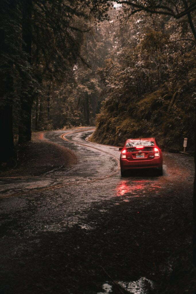 a red car driving on a wet road with trees on either side