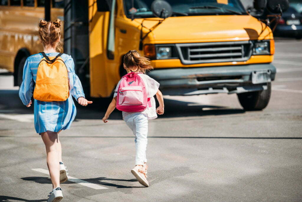 rear view of schoolgirls with backpacks running to school bus